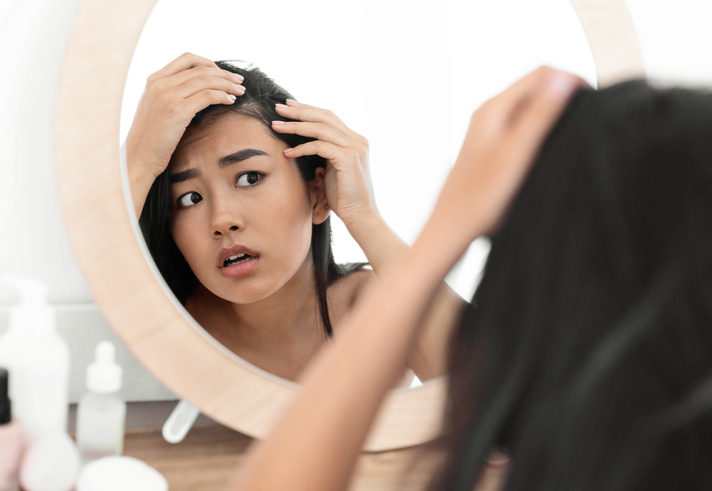 Worried woman checking her hair in mirror at home